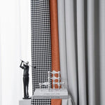 Rideaux modernes et élégants avec différents motifs géométriques, comprenant un design à pied-de-poule noir et blanc, une teinte unie orange et une couleur grise sobre. Accessoire décoratif en métal représentant un golfeur, posé à côté de livres artistiques, créant une ambiance contemporaine dans le salon.