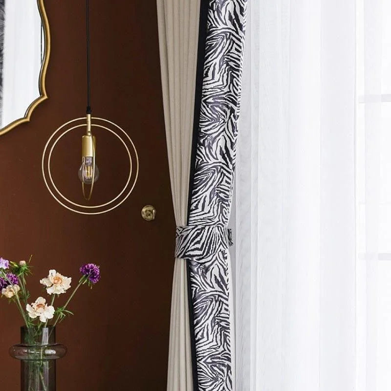 Élégant espace de vie avec rideaux à motif zèbre et éclairage design suspendu. Miroir doré accroché au mur chocolat, vase avec fleurs fraîches ajoutant une touche de couleur. Ambiance moderne et chic pour un intérieur raffiné.