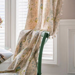 Rideau décoratif avec motifs floraux colorés, suspendu dans une salle lumineuse avec fauteuil et fenêtre à volets. Élément parfait pour ajouter une touche élégante et naturelle à tout intérieur. Accessoire idéal pour embellir votre espace avec des teintes douces et un design raffiné.