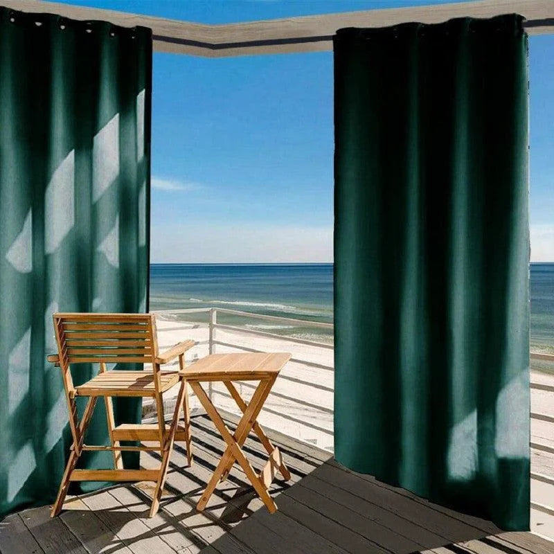 Balcon moderne avec rideaux occultants vert foncé offrant une vue panoramique sur l'océan, accompagné d'un ensemble de mobilier de jardin pliant en bois pour une ambiance détente et élégance extérieure.