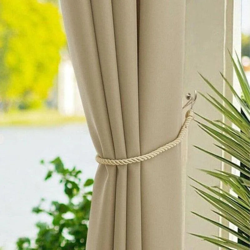 Attache rideau beige élégant avec embrasse en corde, idéale pour décorer le salon ou la chambre. Accessoire pratique offrant un style raffiné à votre intérieur. Fenêtre avec vue sur jardin et plante en premier plan.