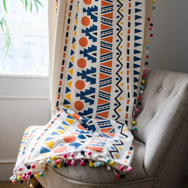 Couverture aux motifs géométriques colorés drapée sur un fauteuil gris, idéale pour ajouter une touche de style bohème à votre intérieur. Décoration élégante et moderne avec des pompons multicolores pour un effet unique. Parfaite pour le salon ou la chambre pour créer une ambiance chaleureuse et accueillante.