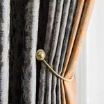 Rideau élégant en tons de gris et orange, image présentant un tie-back doré accrochant le tissu en plis raffinés, parfait pour rehausser l'intérieur de la maison avec une touche de sophistication. Accessoire de décoration idéal pour un salon moderne.