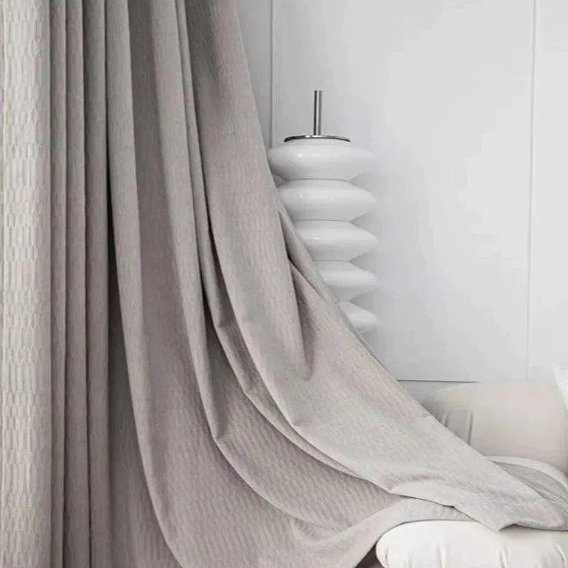 Rideau élégant gris clair tombant gracieusement dans un intérieur moderne de salon. Parfait pour ajouter une touche raffinée et contemporaine à votre espace. Design épuré et esthétique idéale pour améliorer la décoration intérieure.