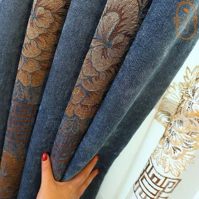Rideau en tissu bleu avec motifs floraux dorés, design élégant pour salon ou chambre, intérieur moderne et chic, main ajustant le rideau.