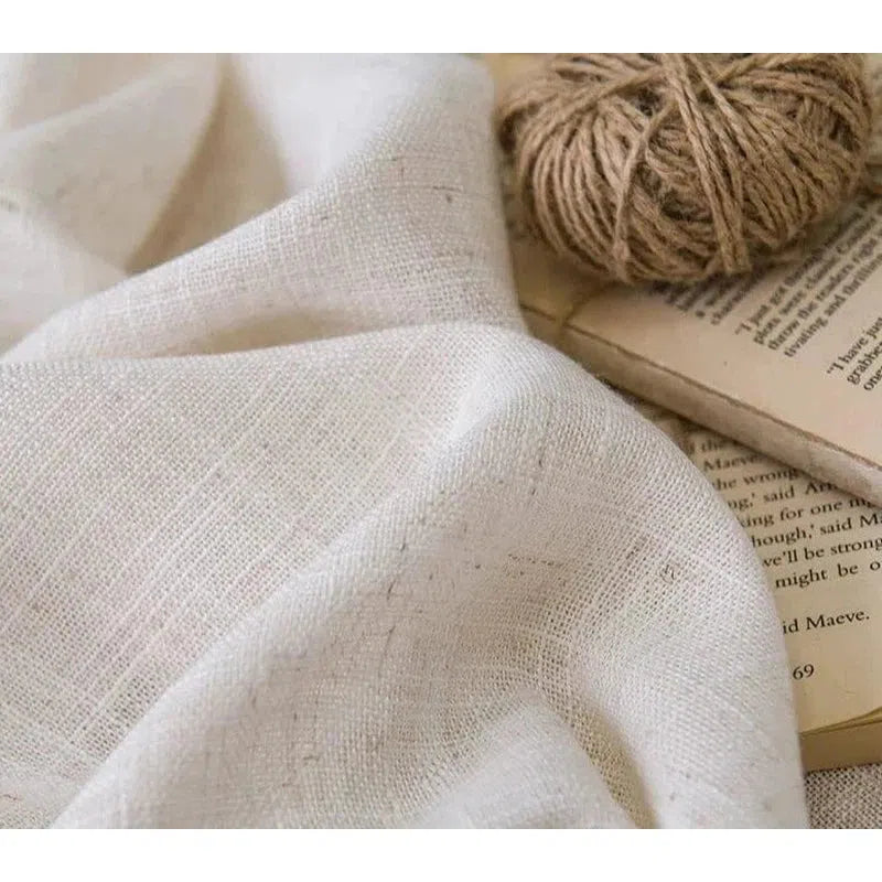 Image d'un tissu blanc doux accompagné d'une pelote de fil, idéal pour des projets de couture ou de décoration intérieure. Le tissu est posé sur un livre, mettant en valeur son élégance et sa versatilité pour l'artisanat et le design. Accessoire parfait pour des créations faites à la main.