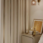 Rideau beige pour chambre élégante, suspendu près d'une table de chevet avec livres, décorations modernes et lampe design, créant une atmosphère chaleureuse et sophistiquée. Idéal pour un intérieur raffiné et contemporain.