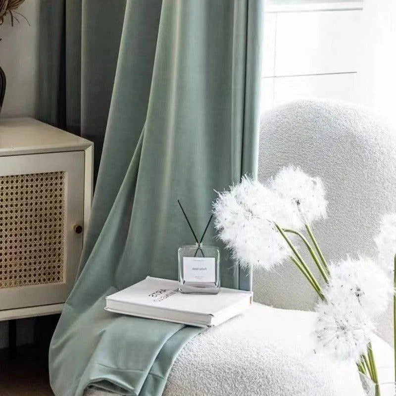 Rideaux élégants vert clair pour salon moderne, complétés par un fauteuil confortable et un meuble en rotin. Ambiance apaisante avec bouquet décoratif et diffuseur de parfum. Idéal pour une décoration intérieure tendance et raffinée.
