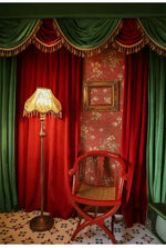 Rideau luxueux en velours rouge et vert avec franges dorées pour décoration intérieure élégante. Ambiance rétro chic avec lampe vintage et chaise en bois rouge. Parfait pour un salon sophistiqué ou un théâtre privé. Design floral sur papier peint pour une touche artistique intemporelle.