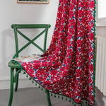 Drapé élégant avec motif floral rouge et bleu, décoré de franges vertes, posé sur une chaise verte vintage. Idéal pour ajouter une touche colorée et romantique à votre intérieur, parfait comme élément décoratif ou couverture légère dans une pièce lumineuse.