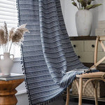 Rideau à motifs géométriques bleu et blanc suspendu près d'une fenêtre lumineuse, créant une ambiance chaleureuse et moderne dans un salon élégant avec des accents naturels. Accessoire décoratif idéal pour habiller vos espaces de vie avec style et raffinement.