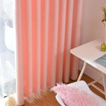 Rideau rose élégant suspendu dans un intérieur moderne, ajoutant une touche de couleur vive à une pièce lumineuse. Ambiance chaleureuse accentuée par un coussin moelleux sur une chaise et une table blanche épurée. Parfait pour décorer un salon ou une chambre.