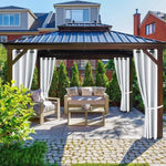 Tonnelle de jardin élégante avec rideaux blancs, offrant un espace détente confortable avec canapé et fauteuil sur une terrasse pavée, entourée de verdure, idéale pour des moments de relaxation en extérieur.