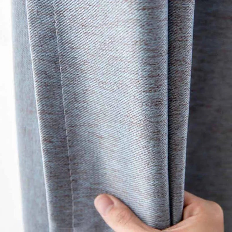 Gros plan d'un rideau épais de couleur grise, présenté par une main tenant le tissu, soulignant la texture et le drapé élégant parfait pour décorer votre intérieur et optimiser la lumière.