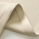 Tissu beige plié, couture visible, gros plan sur la texture douce et uniforme, idéal pour la confection de vêtements ou d'accessoires de mode.