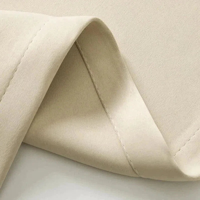 Tissu beige plié, couture visible, gros plan sur la texture douce et uniforme, idéal pour la confection de vêtements ou d'accessoires de mode.