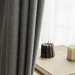 Rideaux élégants gris à motif chevron devant une fenêtre lumineuse avec décoration de livres et bougies, idéals pour une décoration intérieure moderne et sophistiquée.
