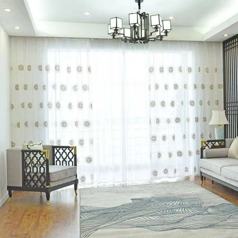 Salon moderne et lumineux avec grandes fenêtres habillées de rideaux élégants à motifs géométriques, espace accueillant avec fauteuils confortables et tapis contemporain, décoration harmonieuse et chic, idéale pour créer une ambiance apaisante et raffinée dans votre intérieur.