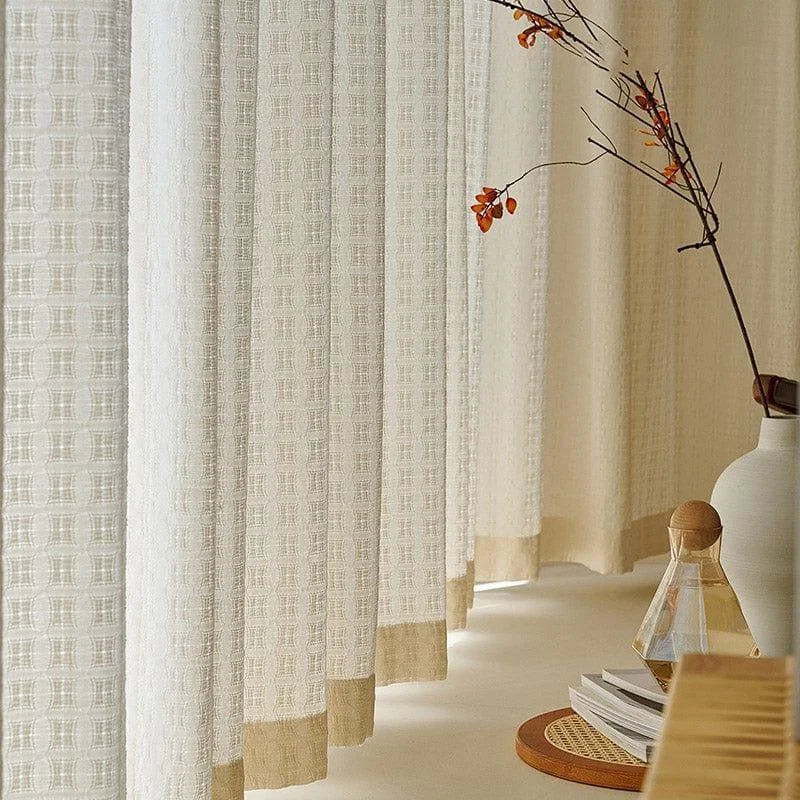Rideaux élégants de couleur claire suspendus dans une pièce lumineuse, apportant une ambiance chaleureuse et raffinée. À côté, une table avec un vase et des livres, ajoutant une touche décorative moderne et minimaliste à l'espace intérieur. Parfaits pour créer une atmosphère paisible et accueillante dans votre salon ou chambre.