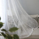 Rideau blanc transparent élégamment drapé sur un canapé gris avec des coussins décoratifs, apportant une touche lumineuse et raffinée à votre salon moderne. Idéal pour filtrer la lumière tout en ajoutant une touche de sophistication à votre espace intérieur. Style chic et intemporel parfait pour une décoration intérieure contemporaine.