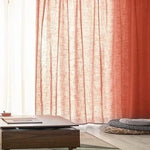 Rideaux rouges élégants filtrant la lumière du jour, idéals pour une ambiance chaleureuse dans le salon. Table basse moderne en bois, entourée de coussins confortables au design unique, parfaite pour une décoration intérieure contemporaine.