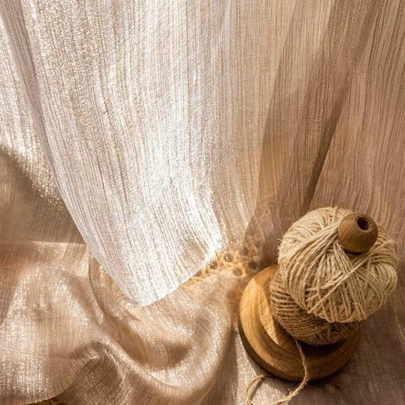 Voilage élégant et lumineux près d'une bobine de fil beige, idéal pour sublimer la décoration intérieure avec une touche chic et naturelle. Parfait pour les salons ou chambres, il apporte une ambiance douce et apaisante grâce à sa teinte chaleureuse et ses reflets scintillants.