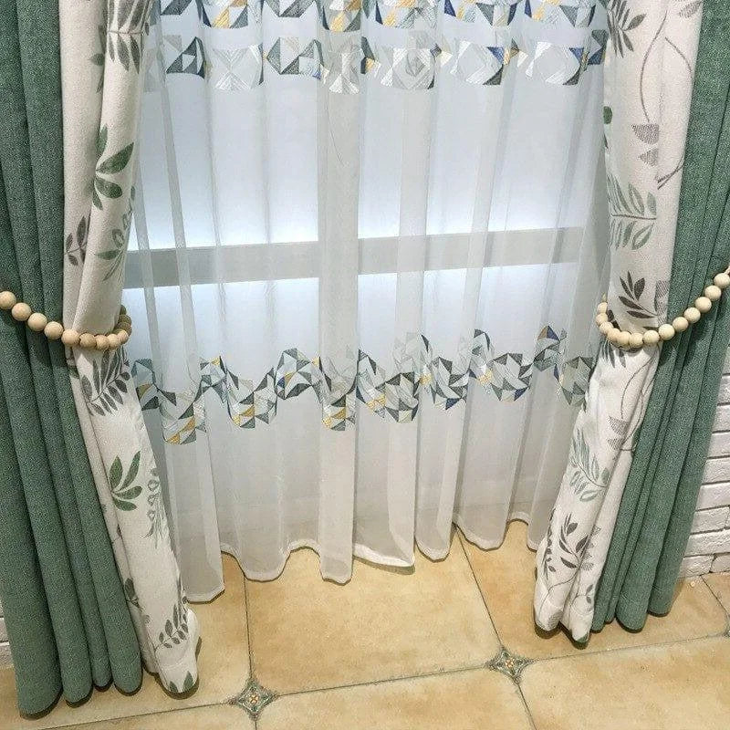 Rideaux élégants avec motifs floraux et géométriques, ornant une fenêtre de salon sur carrelage beige. Harmonisent la décoration intérieure tout en offrant une touche de charme moderne et naturel.