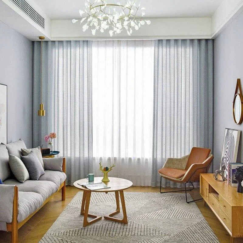 Salon moderne et lumineux avec un canapé confortable, fauteuil design, table basse élégante et rideaux raffinés. Décor minimaliste avec touches de couleur, offrant une ambiance accueillante. Luminaire artistique suspendu, parfait pour un intérieur contemporain. Espace idéal pour la détente et le partage.