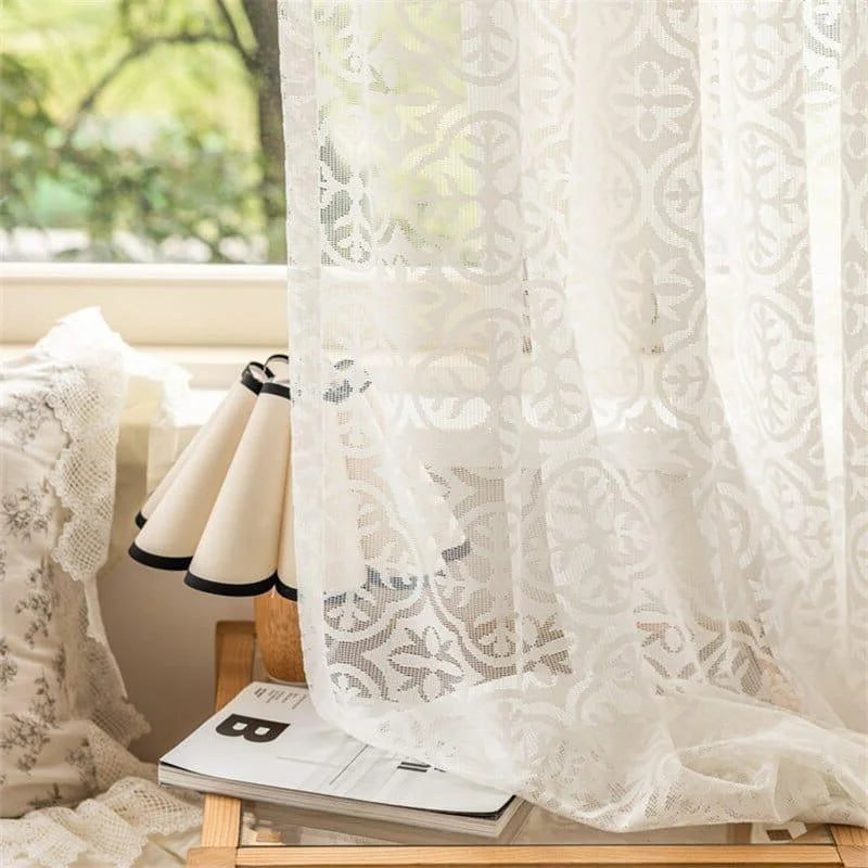 Voilage blanc élégant avec motifs décoratifs suspendu près d'une fenêtre, apportant une ambiance lumineuse et raffinée à votre intérieur. Idéal pour ajouter une touche de charme à votre salon ou chambre à coucher.