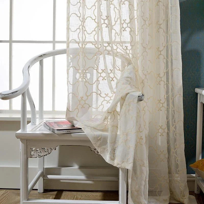 Voilage élégant beige avec motifs géométriques, suspendu près d'une fenêtre lumineuse. Idéal pour une décoration intérieure chic et apaisante. Ajoute une touche de sophistication à votre salon ou chambre, tout en laissant passer une douce lumière naturelle.