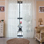 Rideau élégant blanc dans un salon décoré de manière classique avec des détails floraux et un mobilier chic, offrant une ambiance lumineuse et accueillante. La pièce est agrémentée de cadres artistiques, d'une lampe de table et d'un tapis rond. Le rideau, accroché à une large fenêtre, laisse entrer une douce lumière du jour, créant une atmosphère chaleureuse et raffinée.