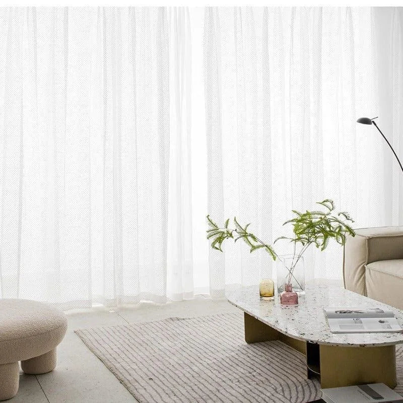 Salon moderne avec table basse design et coussin confortable, rideaux blancs élégants, ambiance lumineuse et épurée, idéal pour une décoration intérieure contemporaine et minimaliste.