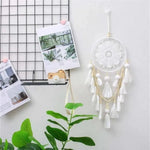 Décoration murale bohème avec capteur de rêves blanc, idéal pour une ambiance apaisante et naturelle. Parfait pour la décoration intérieure, il ajoute une touche tendance et élégante à votre pièce. Accessoire déco suspendu près d'un tableau d'affichage et d'une plante verte.