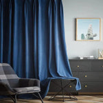 Rideau bleu élégant dans un salon moderne avec un fauteuil à motifs écossais. Décoration intérieure chic comprenant une commode noire, un cadre décoratif et une table d'appoint minimaliste, créant une atmosphère sophistiquée et accueillante.
