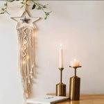 Décoration murale étoile avec franges suspendues, parfaite pour ajouter une touche bohème à votre intérieur. Ornée de petites lumières, elle s'harmonise élégamment avec des bougeoirs modernes disposés sur une table en bois. Créez une ambiance chaleureuse et accueillante dans votre salon ou votre chambre à coucher.