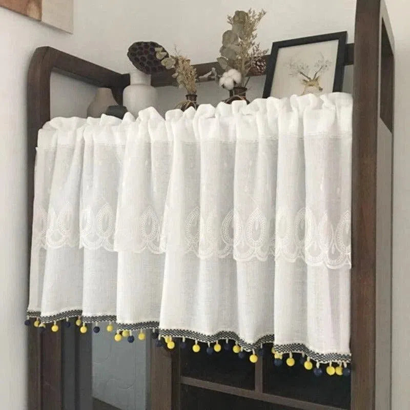Brise-bise blanc décoratif avec broderies élégantes et pompons colorés en jaune et bleu pour habiller vos fenêtres avec style. Idéal pour ajouter une touche de charme à votre intérieur, tout en préservant votre intimité. Convient parfaitement aux cuisines, salons et chambres à coucher pour une décoration harmonieuse et originale.