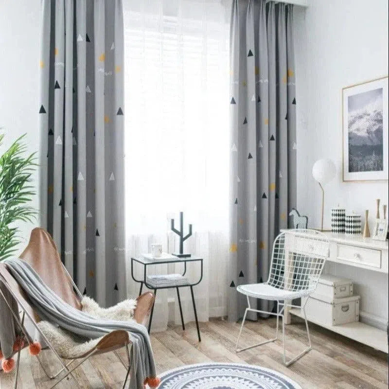 Chambre lumineuse et moderne avec rideaux gris à motifs géométriques, apportant une touche élégante et contemporaine. Espace aménagé avec fauteuil confortable, petite table d'appoint et chaise design, idéal pour un coin lecture ou détente. Ambiance chaleureuse avec décoration minimaliste et parquets en bois clair.