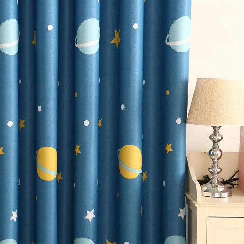 Rideau bleu décoratif avec motif de planètes et d'étoiles, parfait pour une chambre d'enfant. Accessoire idéal pour ajouter une touche ludique et colorée à la décoration intérieure. Style moderne et céleste pour stimuler l'imagination des plus jeunes. Accompagné d'une lampe élégante sur une table de chevet, créant une atmosphère cosy et chaleureuse.