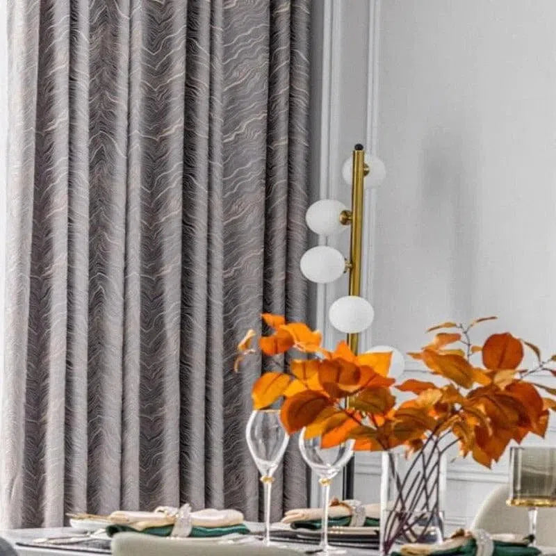 Rideau élégant de couleur grise avec motif subtil, idéal pour une décoration intérieure moderne. Suspendu dans une salle à manger lumineuse, ce rideau apporte une touche sophistiquée et harmonieuse à la pièce. Parfait pour compléter un aménagement avec des accessoires décoratifs contemporains.