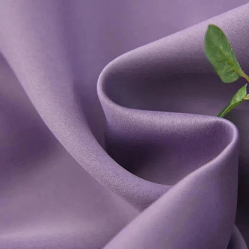 Gros plan sur un tissu violet avec une texture douce, accompagné d'une touche de vert apportée par une feuille, idéal pour la mode et la décoration d'intérieur élégante et moderne.