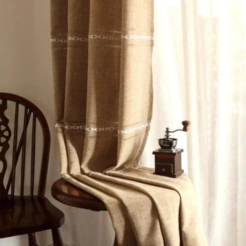 Rideau élégant de couleur beige avec motifs brodés subtils, idéal pour ajouter une touche chaleureuse et accueillante à votre intérieur. Accessoire de décoration parfait pour le salon, la chambre ou la salle à manger, offrant une ambiance cosy. Accessoire complémentaire à côté d'une chaise en bois classique et d'un moulin à café vintage.