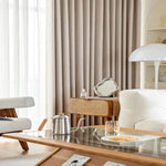 Salon moderne avec rideaux élégants et mobilier scandinave. Un fauteuil confortable et une lampe design complètent ce décor chaleureux. La table basse en verre ajoute une touche sophistiquée, entourée d'un intérieur lumineux et épuré. Idéal pour un style contemporain et accueillant.