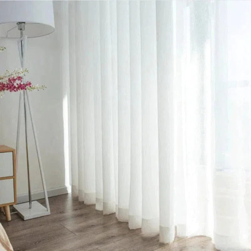 Rideau en voile blanc moderne dans un salon lumineux, offrant une ambiance élégante et épurée. Ce rideau léger et transparent permet de filtrer délicatement la lumière naturelle, tout en préservant l'intimité de votre espace. Idéal pour une décoration intérieure contemporaine.