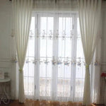 Rideaux élégants blancs sur une grande fenêtre avec un motif floral, ajoutant une touche de sophistication et de luminosité à l'intérieur d'une pièce moderne. Parfaits pour filtrer la lumière tout en décorant le salon ou la chambre à coucher. Idéal pour créer une atmosphère accueillante et stylée.