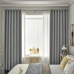 Chambre moderne et élégante avec rideaux opaques gris encadrant une fenêtre lumineuse; lit confortable avec coussins jaunes et gris, créant une ambiance douce et accueillante. Décoration intérieure épurée parfaite pour un espace de détente, combinant style et fonctionnalité.