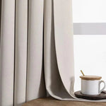 Rideau beige occultant élégant en tissu épais, idéal pour la décoration intérieure moderne. Offre intimité et contrôle de la lumière, parfait pour chambre ou salon. Assorti à une tasse en céramique blanche sur une table en bois clair. Acheter des rideaux de qualité pour un intérieur contemporain et chaleureux.
