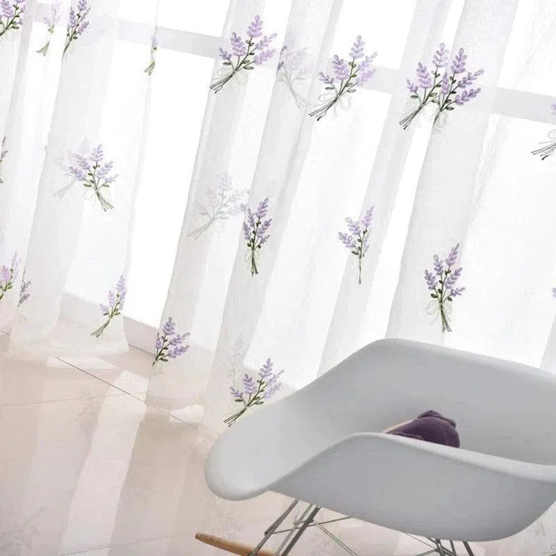 Rideau translucide décoré de motifs floraux lavande, idéal pour embellir un salon moderne. Les voilages permettent de tamiser la lumière tout en ajoutant une touche de nature à votre intérieur. Design élégant et épuré, parfait pour tous les espaces de vie. fauteuil contemporain blanc au premier plan.