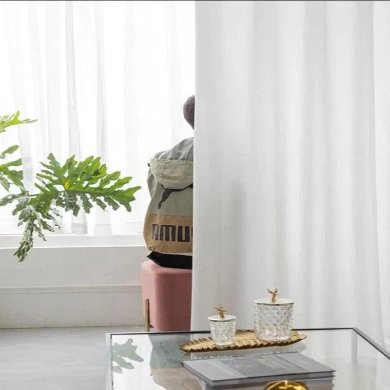 Image d'un espace intérieur moderne et épuré avec une touche de nature grâce à une plante verte. Un tabouret rose et une table basse en verre ornée de bougies ajoutent un charme subtil au décor. Idéal pour l'inspiration en aménagement et décoration d'intérieur.