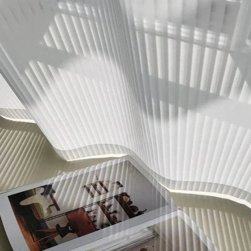 Voilage blanc léger suspendu, créant des jeux d'ombre et de lumière dans une pièce lumineuse. Parfait pour filtrer la lumière naturelle tout en ajoutant une touche esthétique à votre décoration intérieure. Idéal pour un salon moderne ou une chambre calme. Découvrez comment ces rideaux apportent élégance et tranquillité à votre espace.