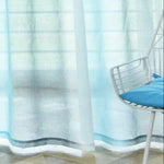 Voilage bleu transparent laissant passer la lumière, idéal pour un salon moderne. Ajoute une touche de fraîcheur à la décoration intérieure, avec une chaise blanche et coussin bleu pour un style épuré et contemporain. Accessoire parfait pour créer une ambiance lumineuse et aérée.
